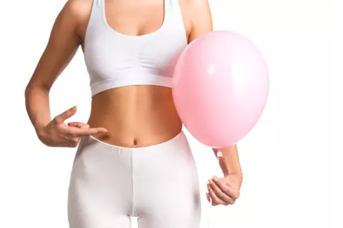 Vrouw in sportoutfit heeft ballon vast en wijst naar haar buik