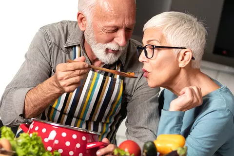 Oudere man laat vrouw van eten proeven tijdens het koken