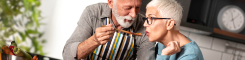 Oudere man laat vrouw van eten proeven tijdens het koken