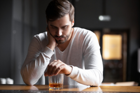Man kijkt neerslachtig naar glas alcohol